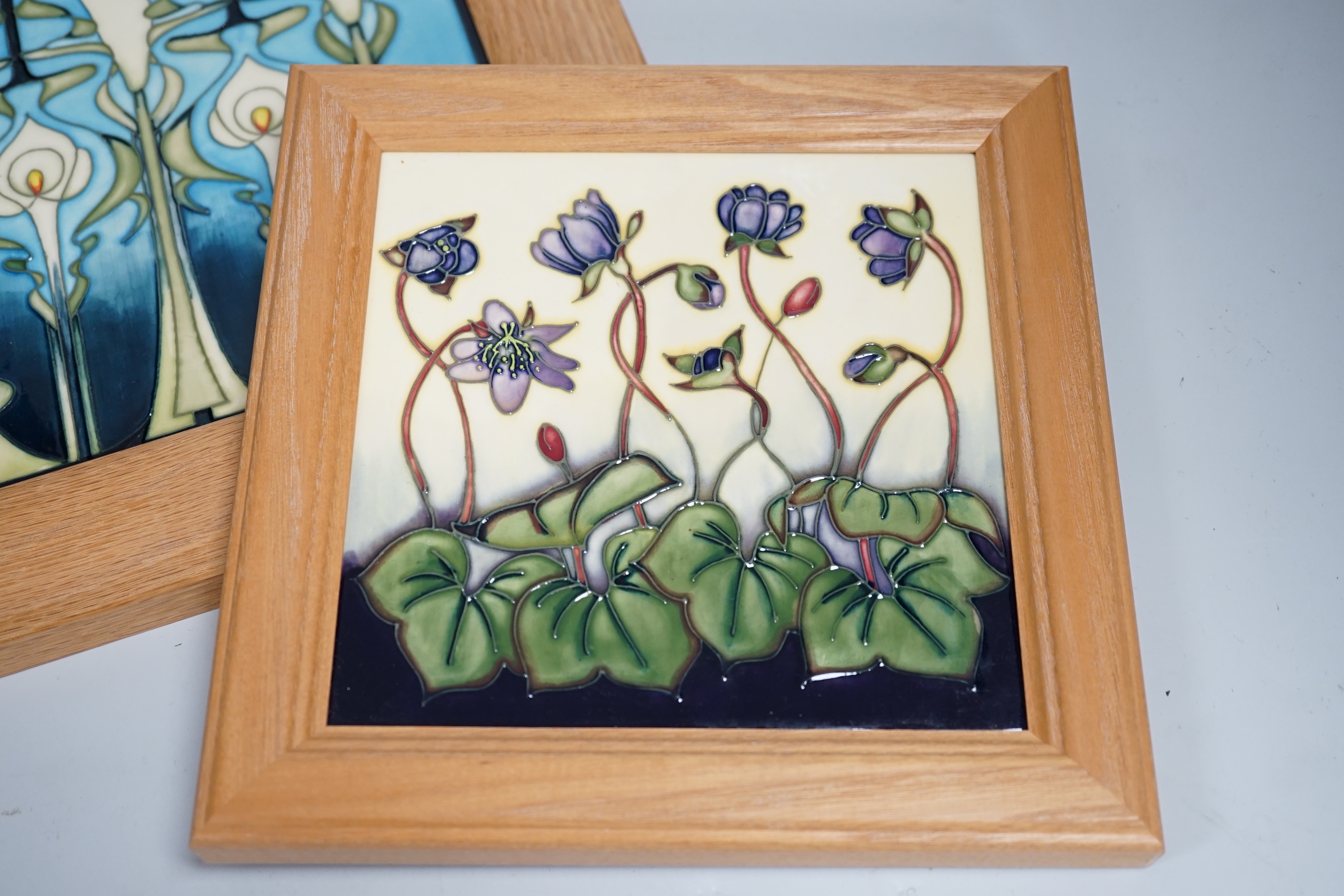 Two framed Moorcroft tiles, one with stylised lilies, the smaller tile with cyclamen, larger tile 21.5cm x 21.5cm